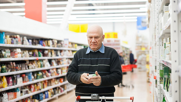 Älterer Mann im Supermarkt guckt auf Packung in seiner Hand