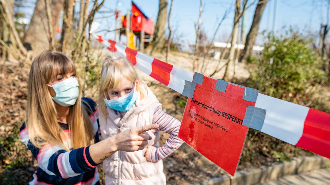 Mutter und Kind stehen vor einem gesperrten Spielplatz. 