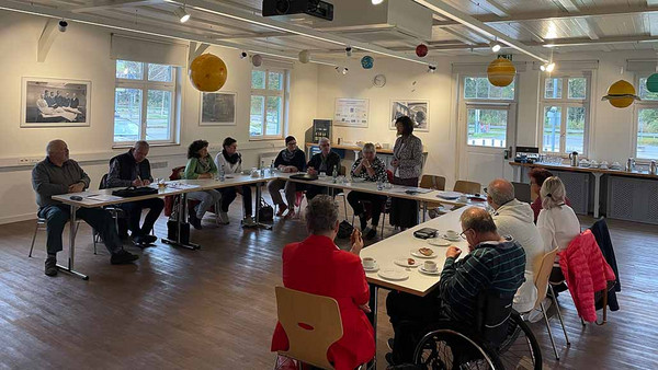 Menschen sitzen im Halbkreis an Tischen