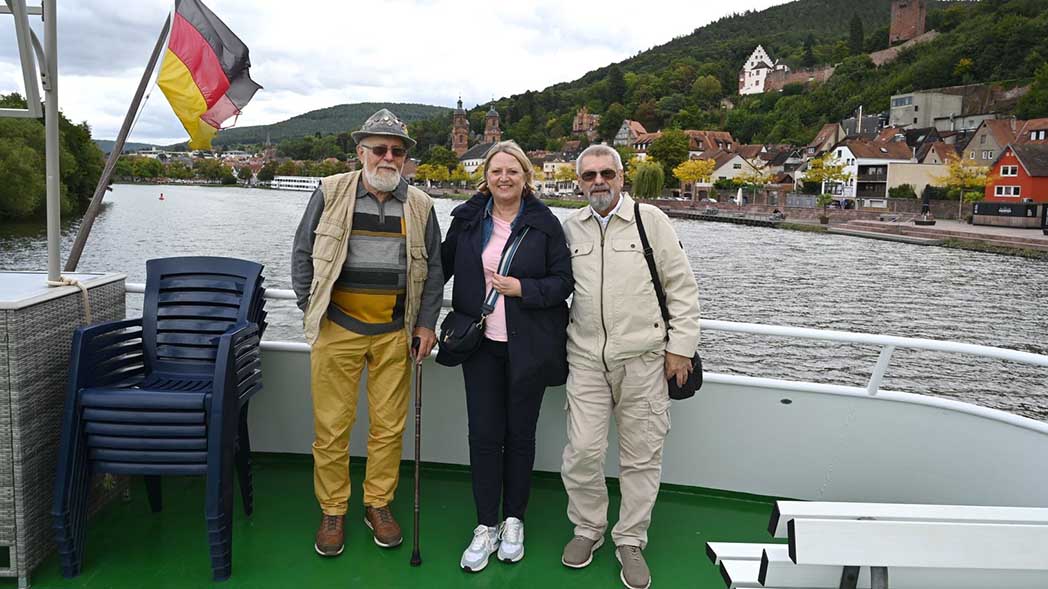 Zwei Männer und eine Frau auf einem Schiffsdeck.